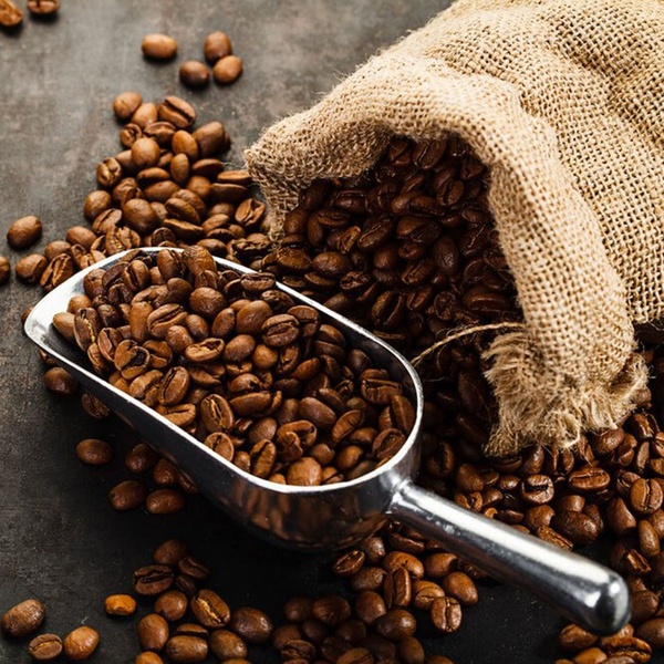 A high-fidelity hero image featuring a burlap sack of premium coffee beans spilling into a metallic scoop on a textured surface.