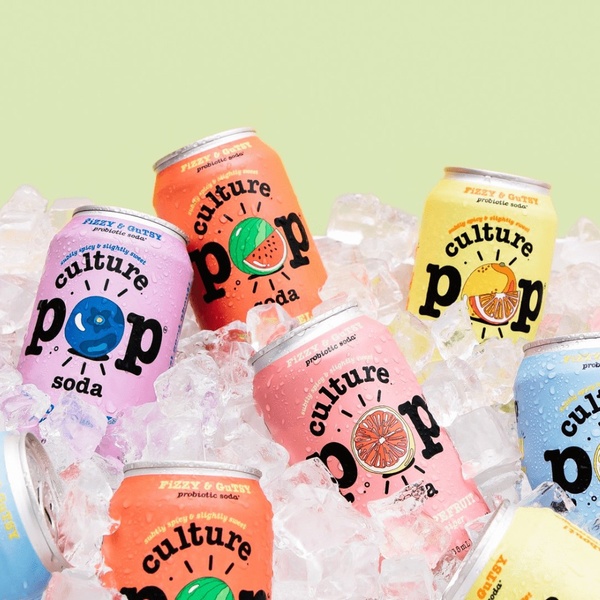A top-down, square composition featuring multiple cans of probiotic soda nestled in a bed of crushed ice, emphasizing temperature and variety.