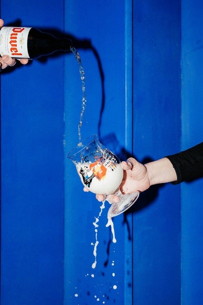 A high-contrast, action-oriented shot showing a beer bottle pouring into a branded glass against a vibrant blue backdrop.
