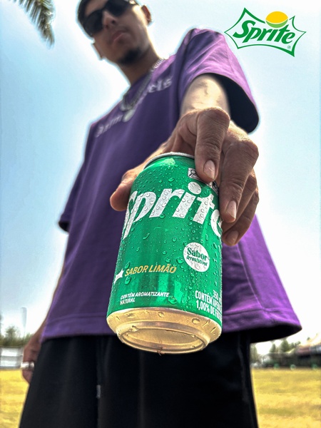 A high-energy, low-angle perspective shot featuring a person offering a cold can of lemon soda to the viewer, emphasizing product condensation and brand recognition.