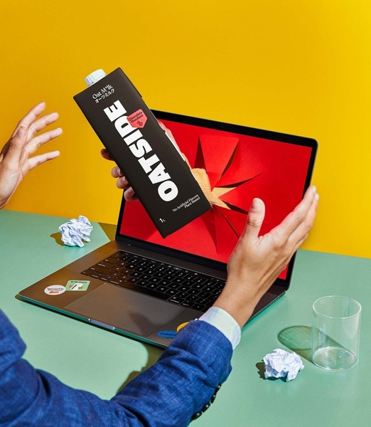 A creative featuring an oat milk carton emerging from a laptop screen, emphasizing the product as a digital-first lifestyle staple.