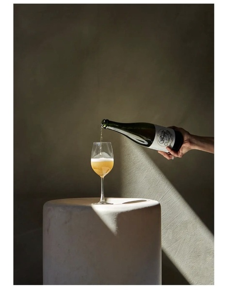 A high-end, dramatic studio shot featuring a sparkling wine being poured into a stemmed glass, illuminated by a single, sharp light beam.