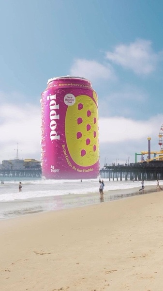 A massive soda can floats above a beach, dwarfing the beachgoers to create a surreal, attention-grabbing visual.