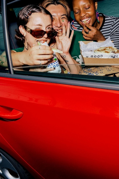 A close-up shot of three diverse friends laughing while eating burritos inside a car, emphasizing shared experiences and casual enjoyment.