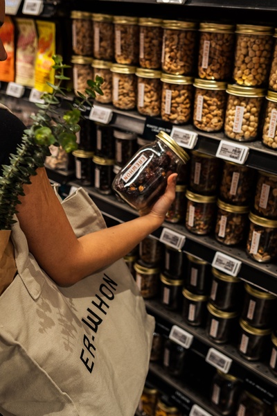 A close-up, first-person perspective showing a shopper selecting a high-quality glass jar of nuts from a well-organized grocery shelf.