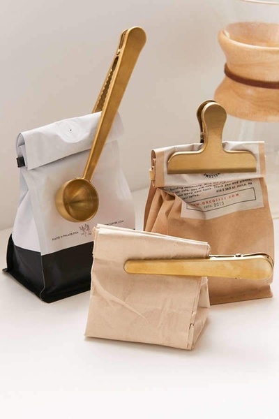 A clean, high-end product showcase featuring brushed gold coffee scoops and clips, using negative space to emphasize quality and premium design.