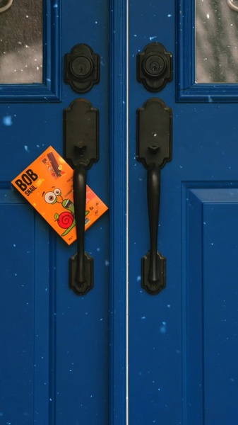 A high-contrast, vertical shot of a vibrant orange fruit bar box hanging on a blue door handle during a light snowfall.