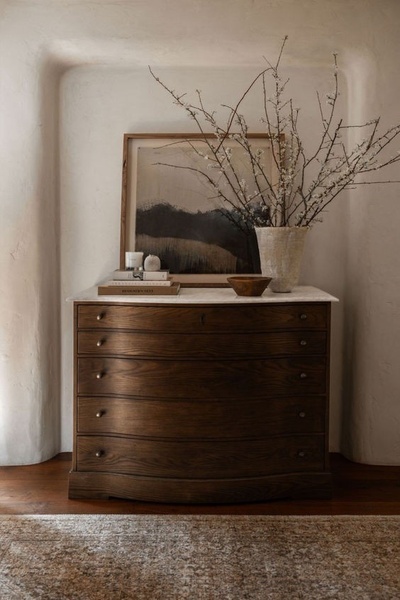 This creative showcases a dark wood dresser in a curved niche, styled with natural decor elements to create an aspirational atmosphere.