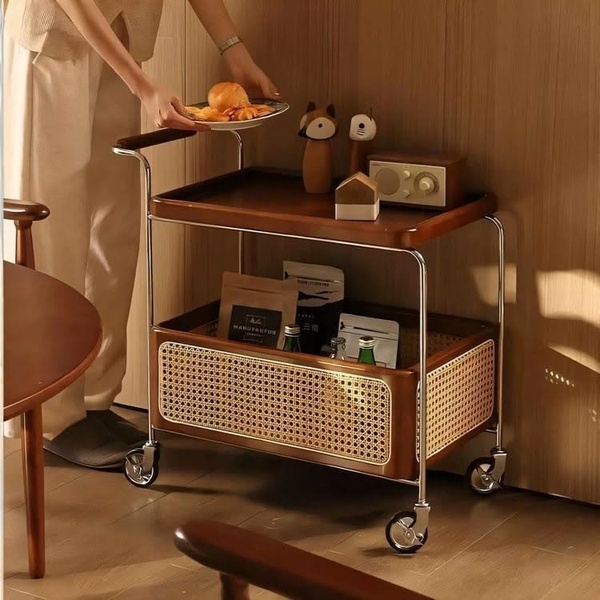 A high-quality lifestyle photograph of a wooden serving cart with rattan detailing, styled with curated home accessories to evoke an aspirational living environment.