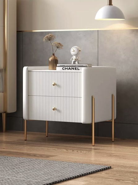 A high-end product hero shot featuring a modern white-fluted nightstand with gold accents in a sophisticated, minimalist bedroom setting.