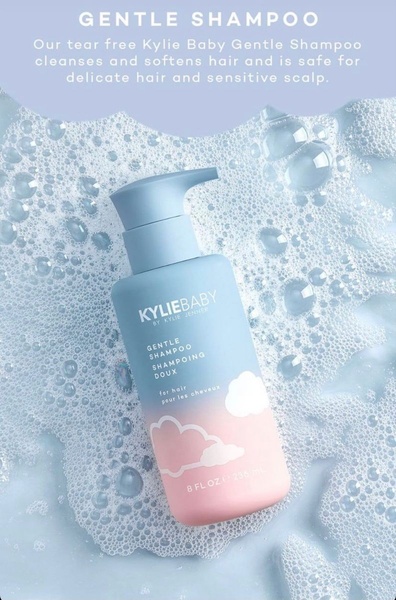 A clean, high-angle product shot of a gentle shampoo bottle submerged in a light-blue bubble bath, using a soft, pastel color palette to communicate safety and comfort.