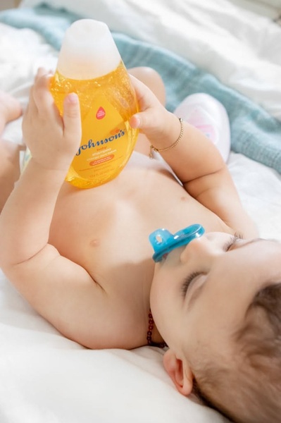 A close-up, soft-focus lifestyle image of an infant holding a bottle of baby shampoo, emphasizing brand trust and product purity.