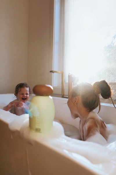 A high-conversion lifestyle shot featuring a baby shampoo bottle in the foreground while children play in a sunlit bathtub.