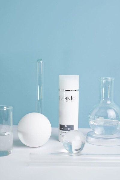 A clean, clinical presentation of a shampoo bottle surrounded by laboratory glassware on a soft blue background.