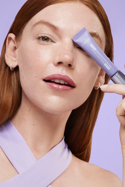 A clean, color-coordinated product hero shot featuring a firming cream held near the face to draw attention to the brand and skincare benefits.