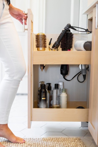 A high-quality lifestyle shot showing a clean, organized bathroom pull-out drawer loaded with neatly stored hair tools and products.