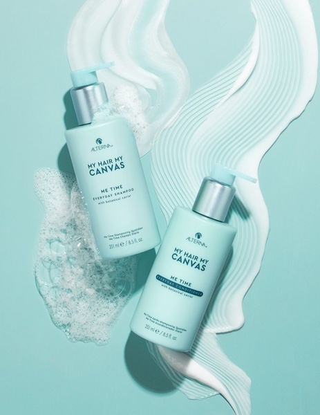 A high-key, minimalist product shot featuring shampoo and conditioner bottles set against a matching teal background with artistic foam swirls.