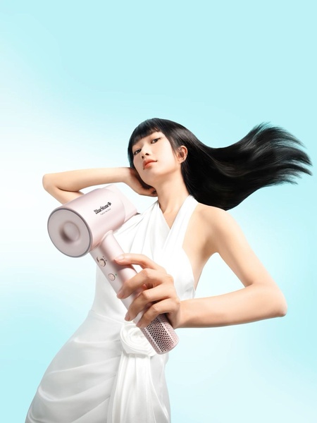 A clean, studio-lit portrait featuring a model holding a sleek, light-pink hair dryer, using a soft pastel color palette to communicate premium quality.
