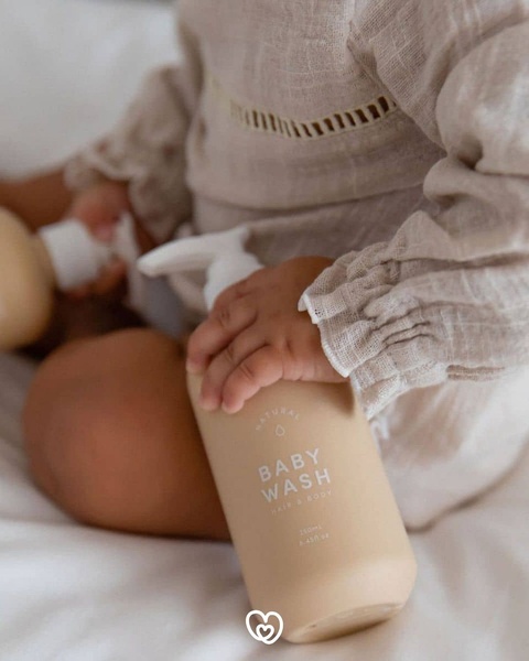 A close-up, soft-focus lifestyle image of a baby holding a bottle of natural baby wash, emphasizing purity and gentle care.