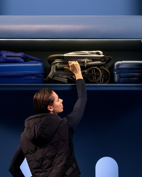 A traveler effortlessly places a folded compact stroller into an airplane overhead compartment, demonstrating its portability and travel-friendly design.