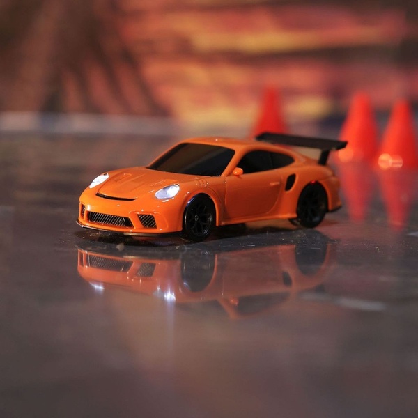 A close-up studio shot of an orange diecast sports car model featuring functional LED headlights and a dramatic orange-lit background.