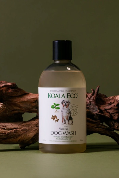 A clean, studio-lit shot of a natural dog wash bottle placed against organic driftwood and an earthy green background.