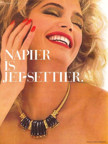 A close-up studio shot of a model wearing a bold gold and black statement necklace, emphasizing a high-end, aspirational lifestyle aesthetic.