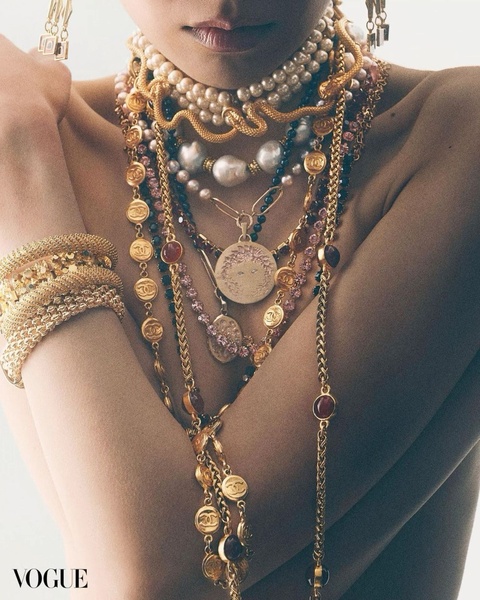 A close-up fashion editorial shot focusing on layered gold necklaces and pearl strands worn against a bare neck.