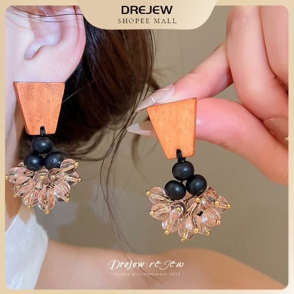 A close-up shot of a pair of unique wooden and bead earrings being held by hand to show size and texture.