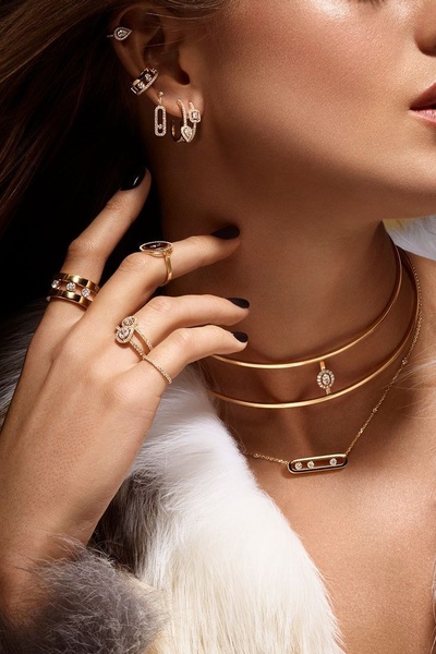 A high-end, close-up shot focusing on layered gold jewelry, including necklaces, rings, and earrings, against a textured white fur background.