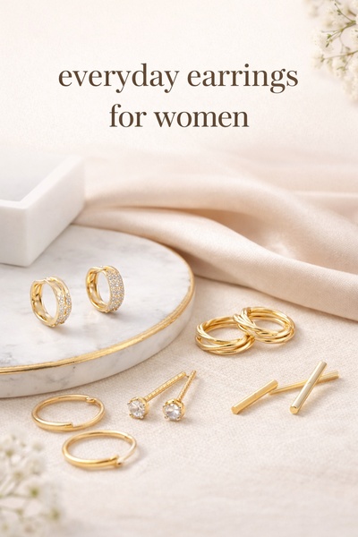 A high-end, clean product flat-lay featuring a curated selection of gold-toned earrings on a white marble and silk backdrop.