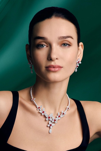 This creative features a professional studio close-up of a model wearing a sophisticated diamond and ruby necklace against a deep green backdrop.