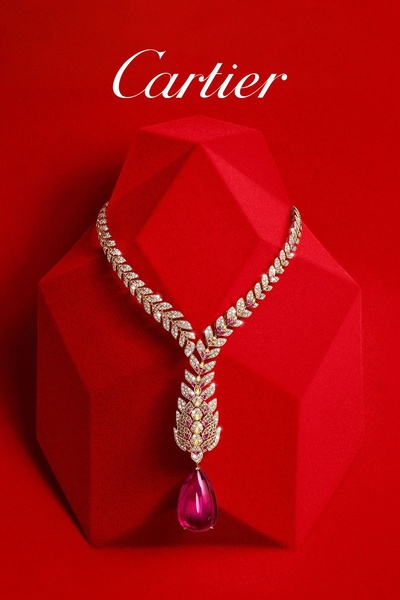 A high-end studio product photograph featuring a diamond and gemstone necklace displayed on a geometric red pedestal.