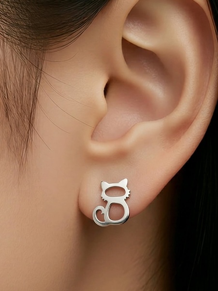 A clean, high-contrast close-up shot focusing on a small, silver cat-shaped earring worn on an earlobe.