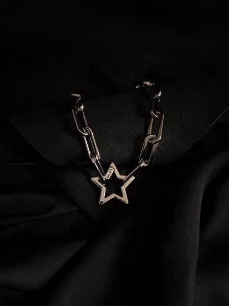 A high-end, cinematic close-up shot of a silver star link necklace draped over dark, textured fabric.