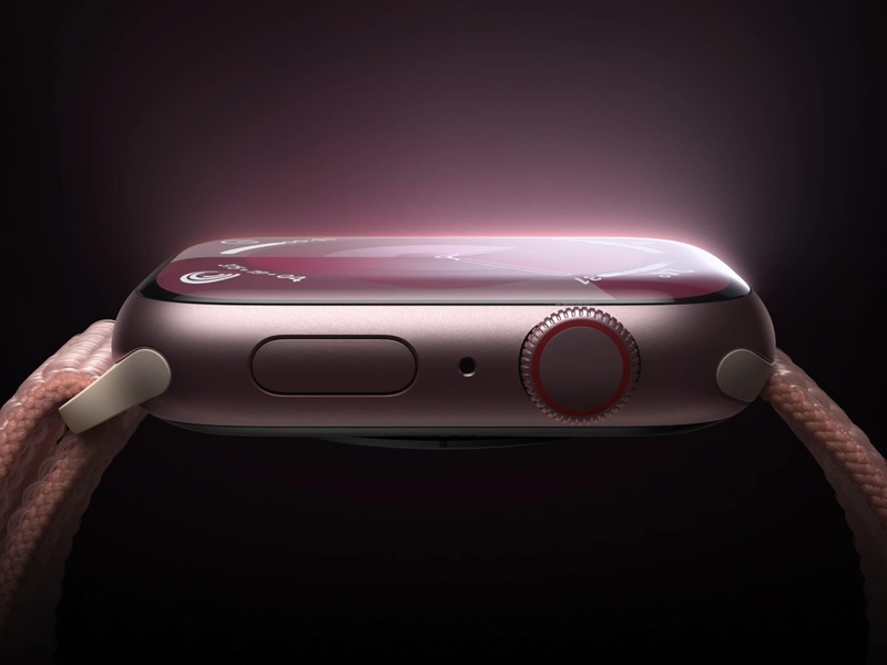 A close-up, side-profile view of a smartwatch featuring a rose-gold casing and textured fabric strap against a dark, moody gradient background.