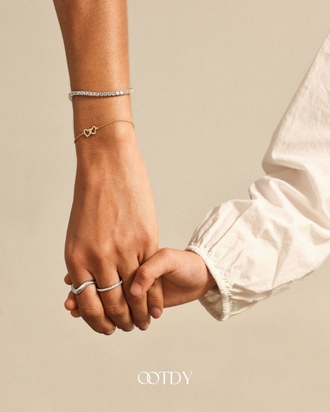 A close-up, high-fashion shot featuring a delicate bracelet and ring set on an individual's hand against a neutral, warm background.