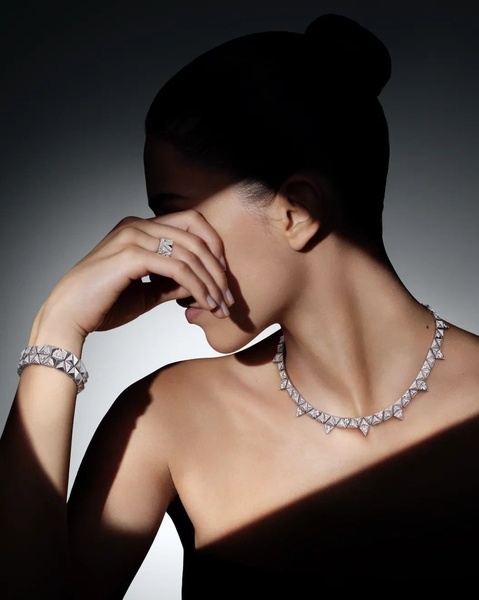 A high-end editorial shot featuring a model wearing a diamond geometric necklace and bracelet, utilizing harsh diagonal lighting to highlight texture and brilliance.