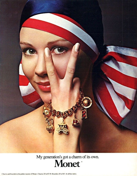 A close-up portrait of a woman wearing a red, white, and blue headscarf, using her hand to frame her face while showcasing an ornate gold charm bracelet.