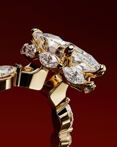 An extreme macro, high-gloss close-up of a luxury diamond ring with multiple cuts, highlighting the metal and gem precision against a deep red background.