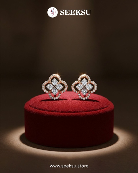 A high-end, studio-lit photograph of diamond stud earrings presented on a red velvet display cushion against a dark, moody background.