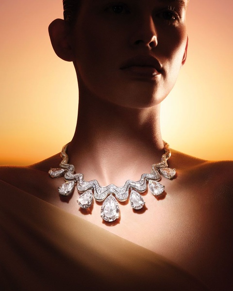 A high-end portrait focus on a pear-cut diamond necklace against a warm, gradient sunset background to evoke exclusivity and grace.