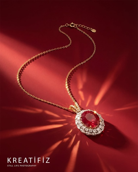 A high-end studio still life shot of a ruby and diamond pendant, featuring dramatic light rays on a rich red background.