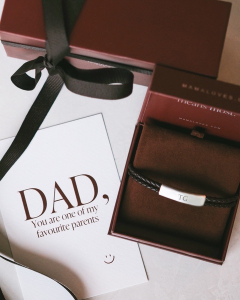A high-end, top-down view of a personalized leather bracelet inside an elegant gift box next to a sentimental handwritten note for a father.