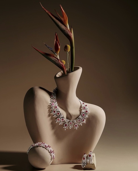 A high-end studio capture featuring a ruby and diamond necklace, bracelet, and earrings displayed on a minimalist sculptural bust with botanical accents.