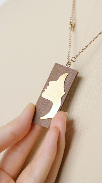 A close-up, high-quality shot of a wood and gold pendant being held by a hand, emphasizing the texture and material contrast.