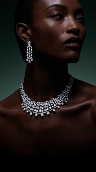 A high-fashion, dramatic close-up shot featuring a model wearing a diamond necklace and matching earrings against a dark, moody background.