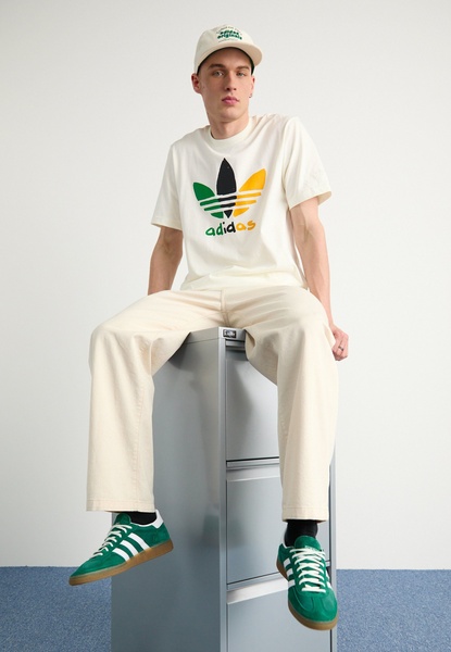 A high-quality lifestyle portrait featuring a model sitting on a clean office pedestal wearing vibrant green sneakers.