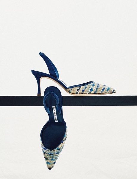 A high-end product hero shot featuring a pair of slingback heels balanced on a thin, dark horizontal shelf against an expansive white background.