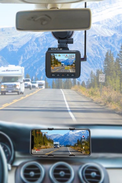 This creative demonstrates a dash cam in use by showing a dual perspective: the driver's front-facing view and a mobile device interface for secondary control.